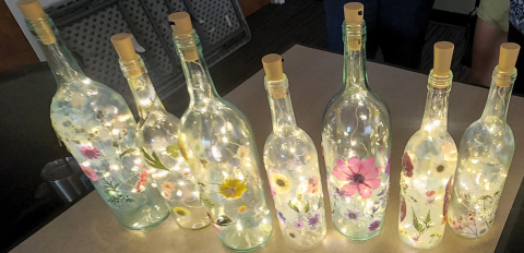 A line of wine bottles that have been mod podged and fairy lights inserted in them. 