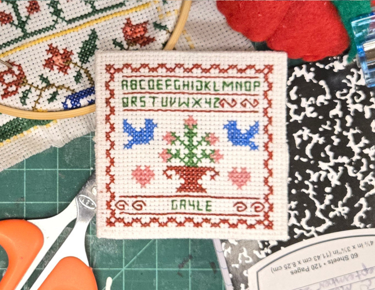 a small stitch sampler featuring the alphabet and two birds. 