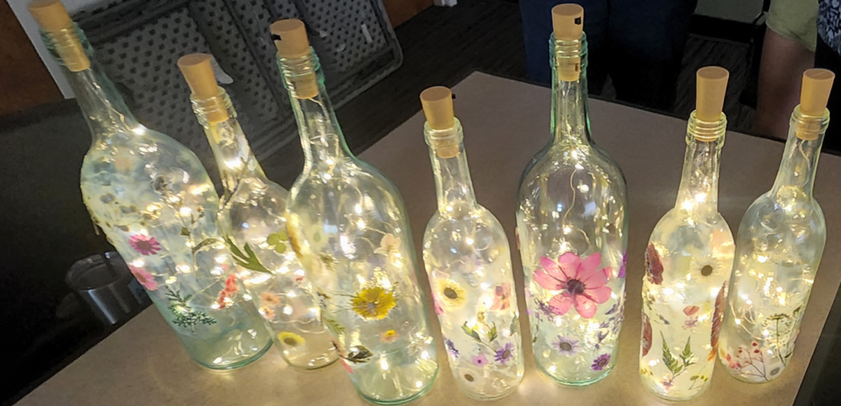 A line of wine bottles that have been mod podged and fairy lights inserted in them. 